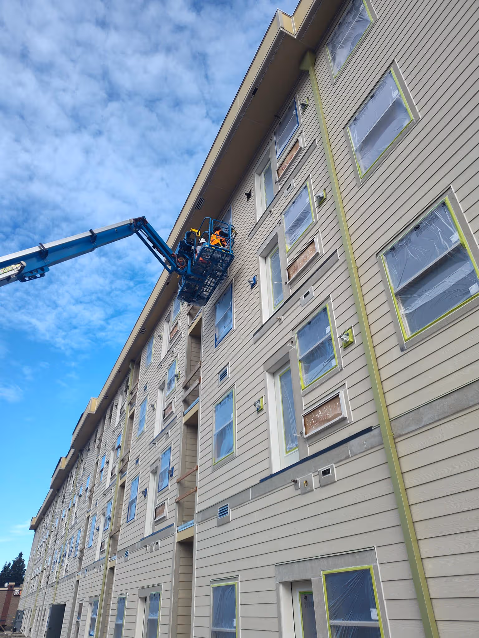 Worker in a lift basket working on the exterior of a large multi-story building under construction.