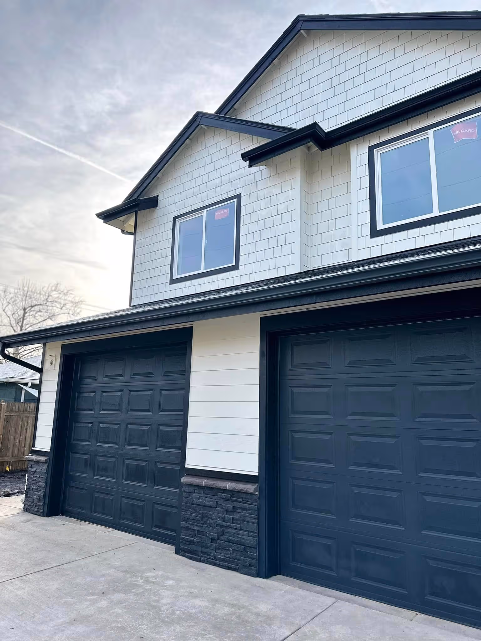 Two closed black garage doors on a white house with black trim and stone accents on the lower walls.