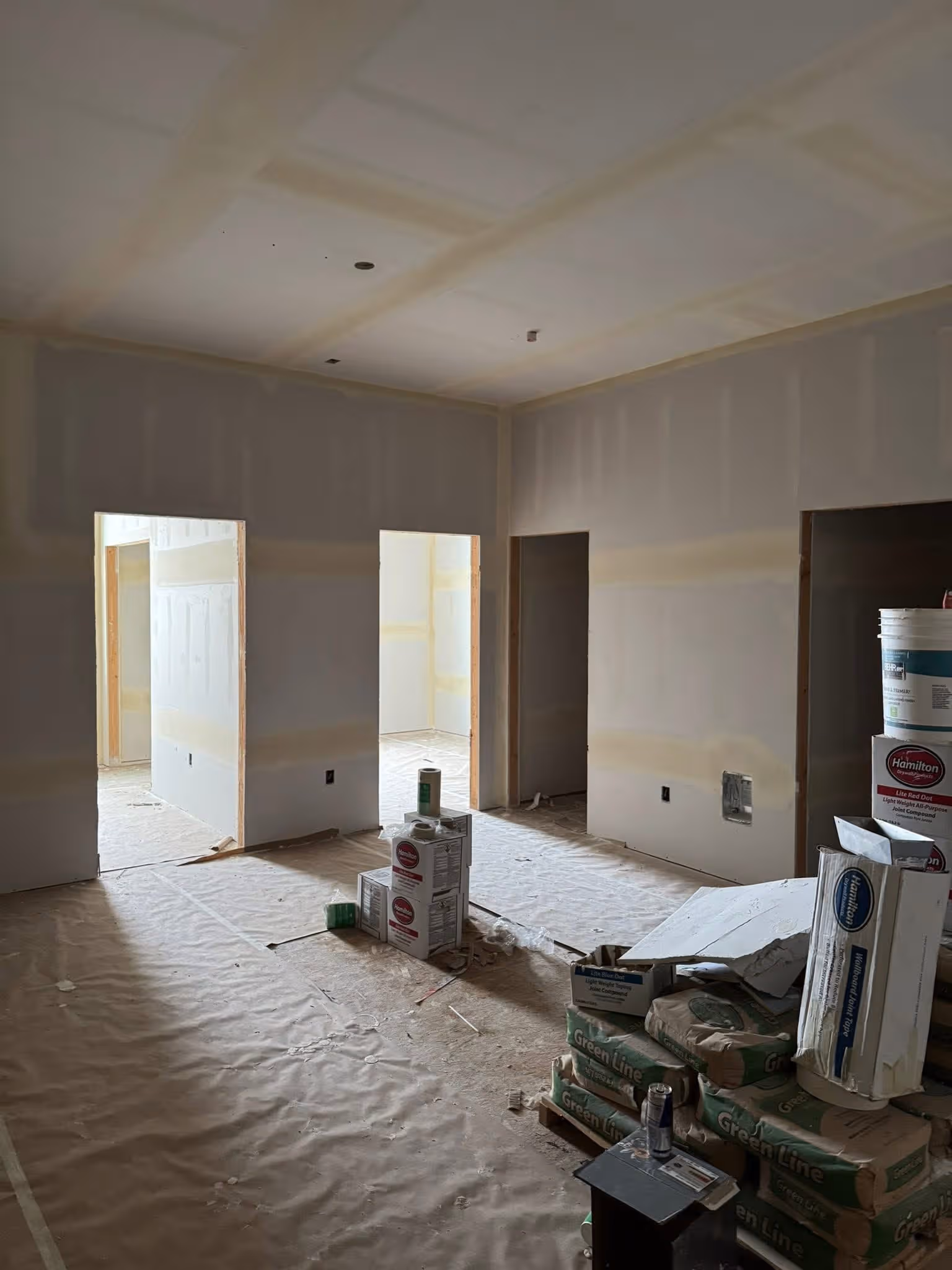 Interior of a room under construction with drywall, stacks of Green Line bags, and paint supply boxes.