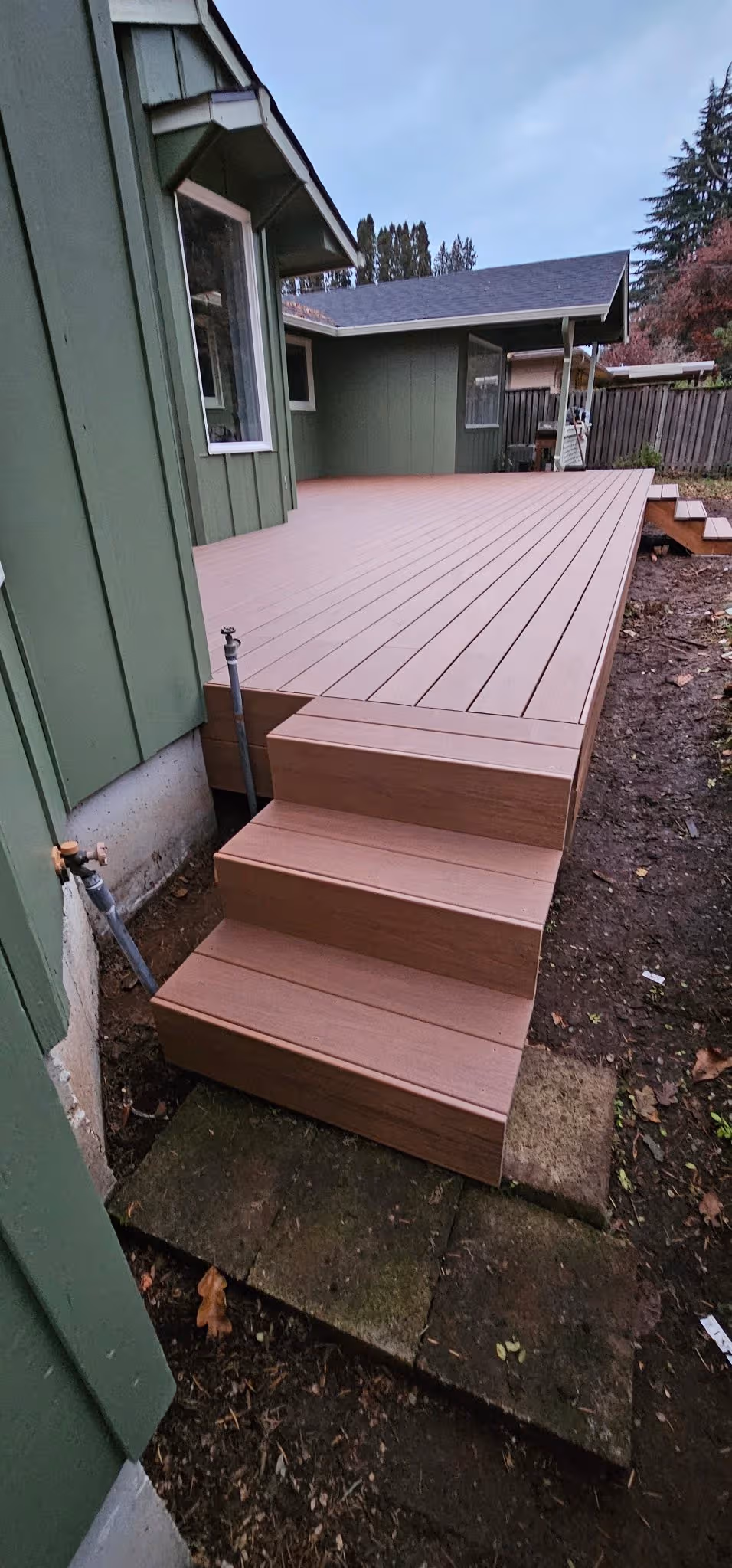 Newly built brown wood composite deck with steps attached to a green house exterior.